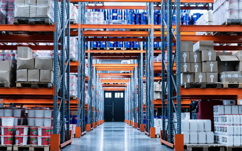 Warehouse aisle with orange pallet racking stocked with pails and cartons